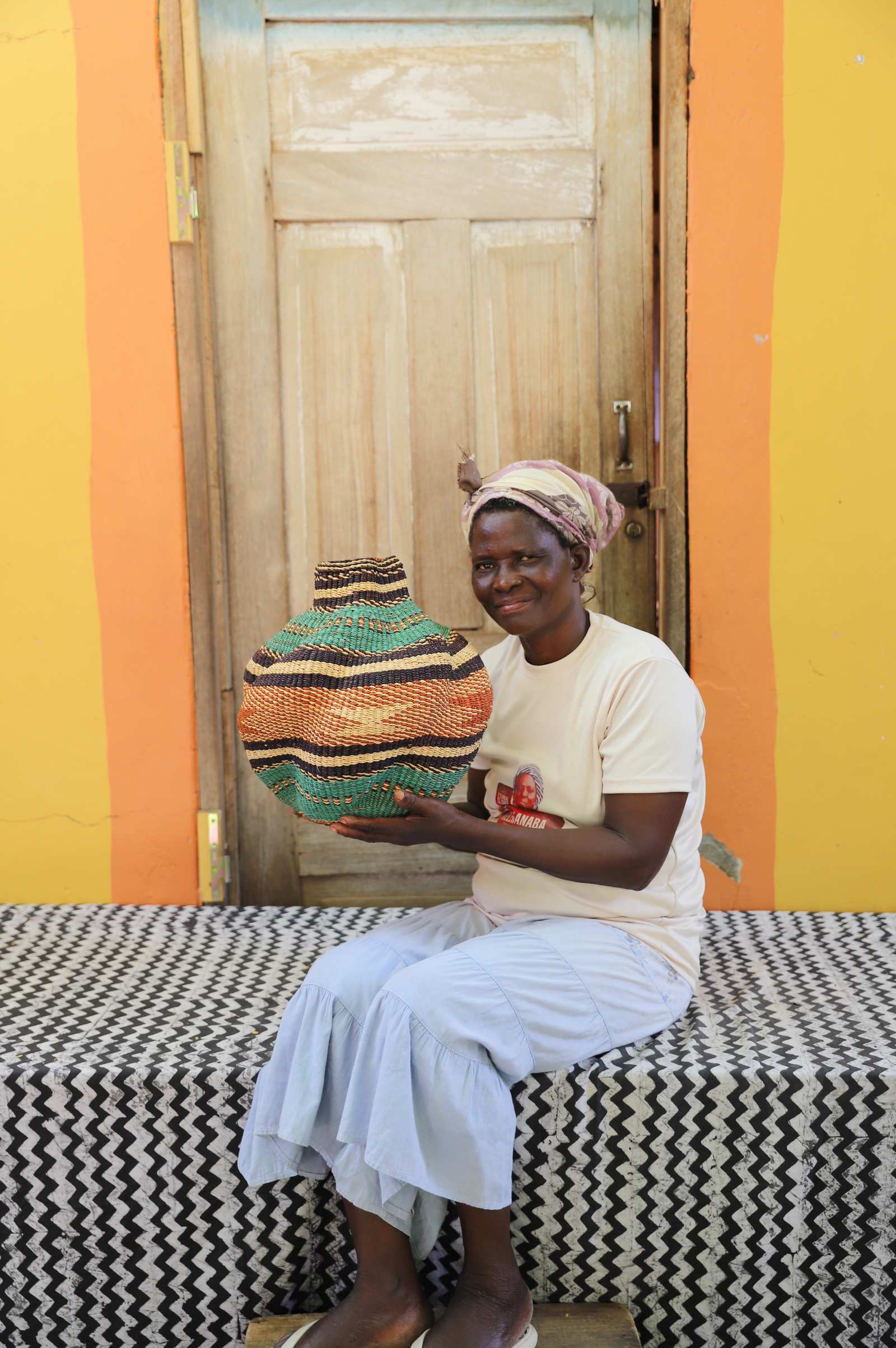 Handwoven Bolga art basket in natural straw with dark bands and red centre, held by a seated woman in white.