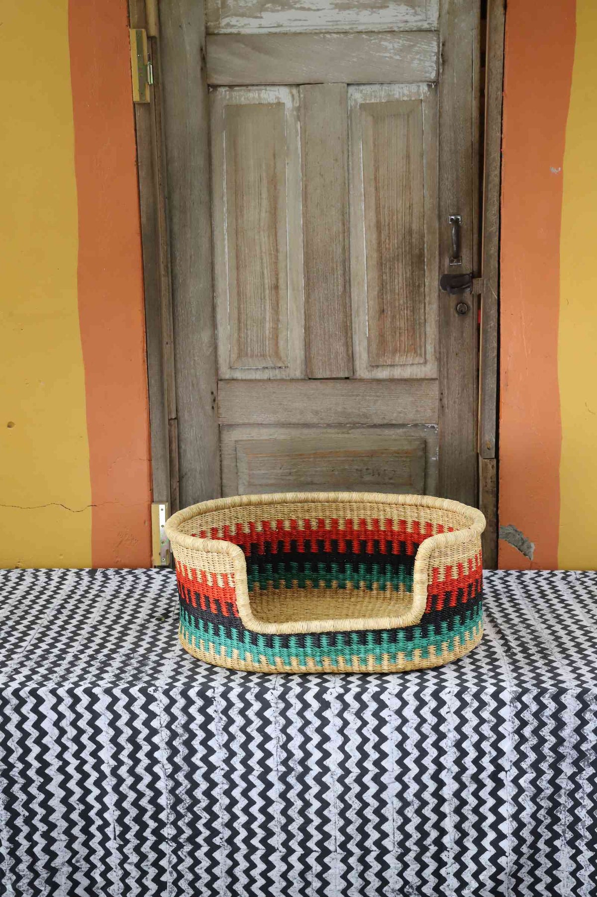 Small handwoven Bolga pet bed in natural straw with red, green and yellow vertical stripes and a green rim.