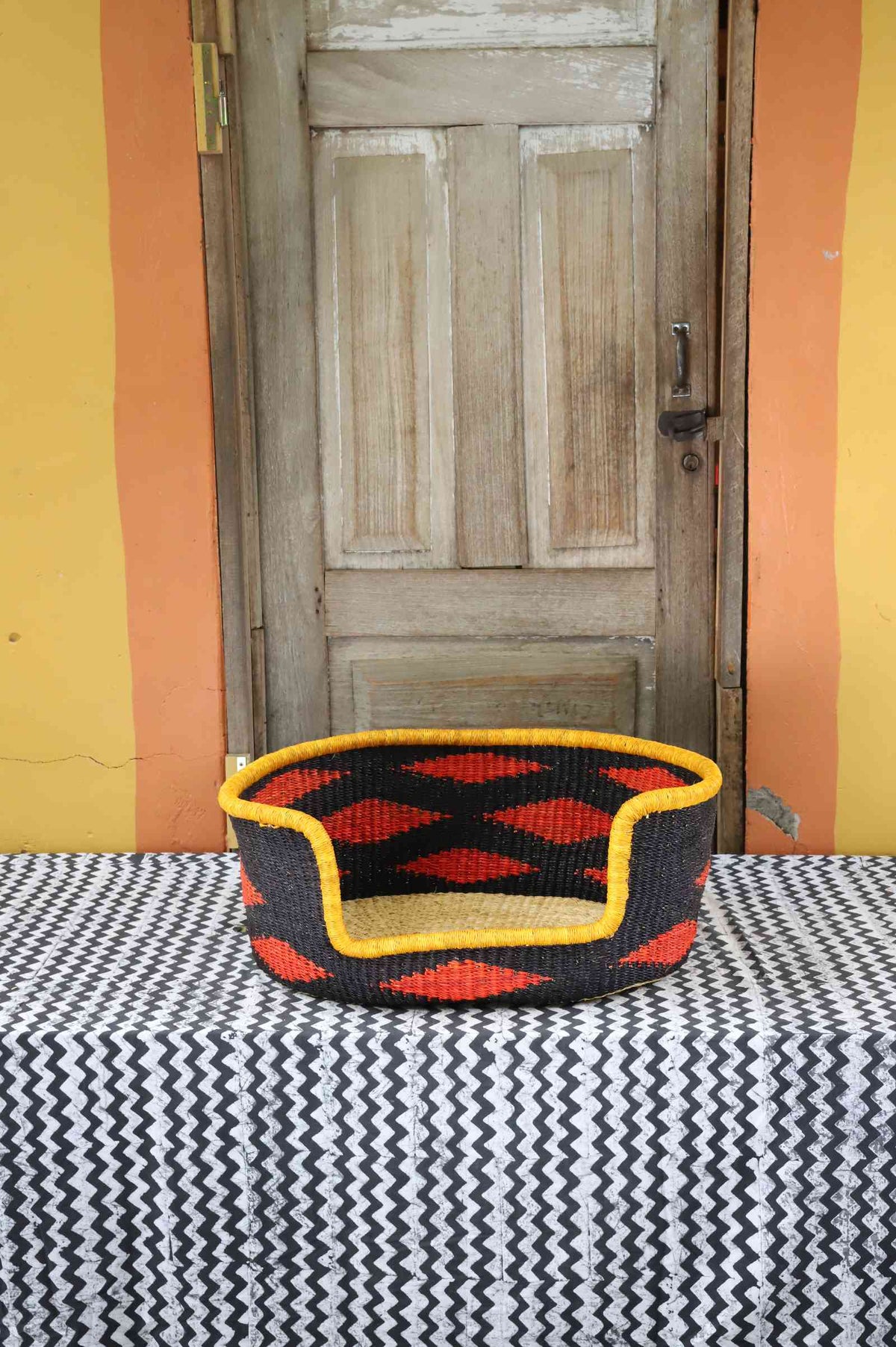 Small handwoven Bolga pet bed in bold black with orange diamond pattern and yellow rim.