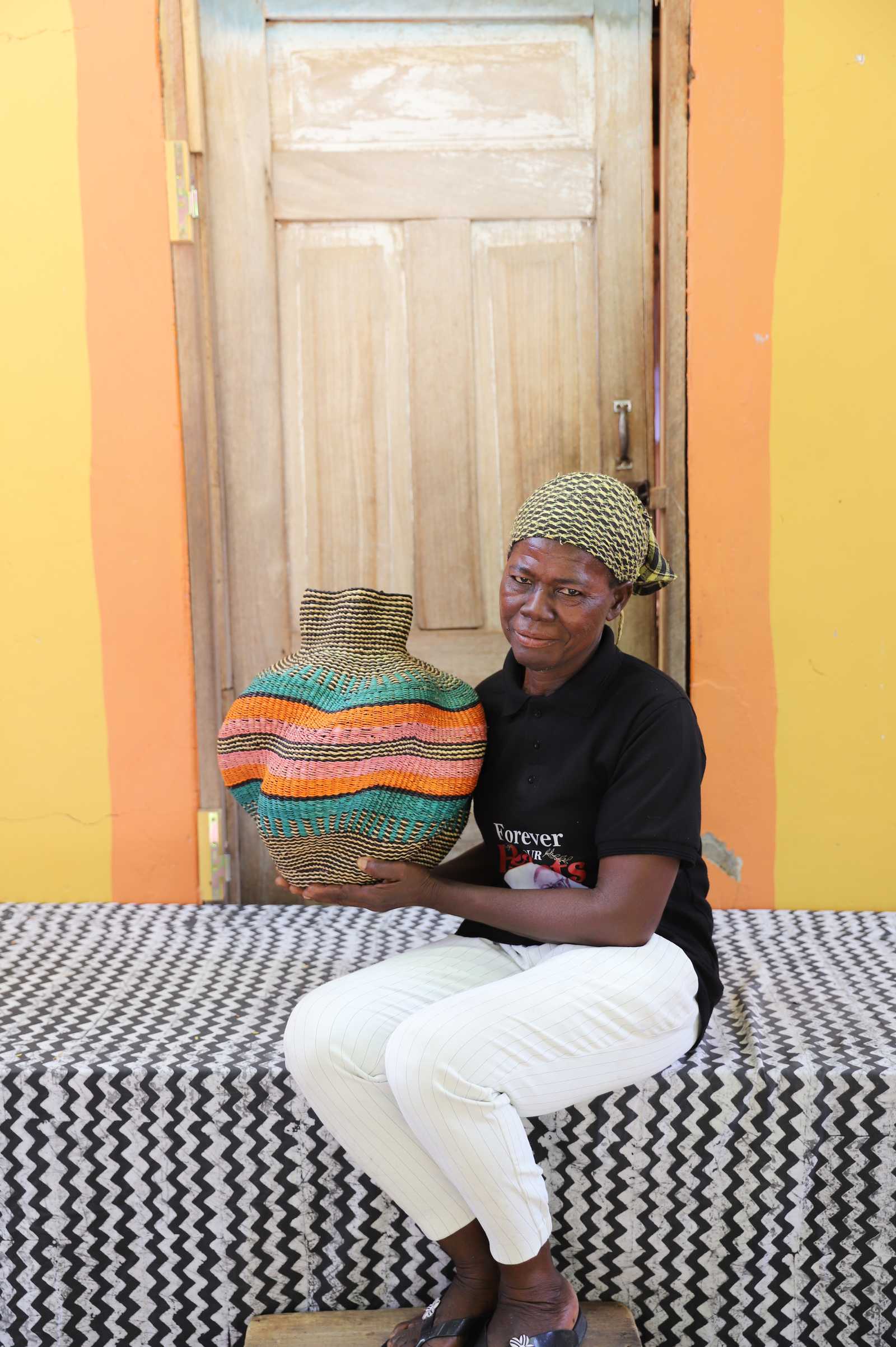 Handwoven Bolga art basket with orange and teal central bands, held by a seated woman in black.