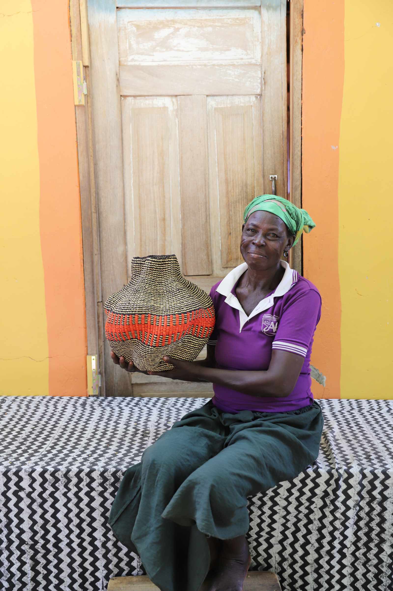 Handwoven Bolga art basket in natural straw with a bold red central band, held by a seated woman in purple.