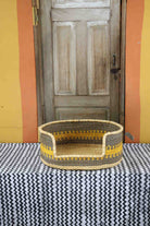 Medium handwoven Bolga pet bed in natural straw with fine yellow banded stripes and a dark rim.