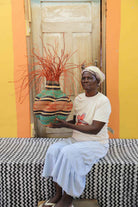 Handwoven Bolga Baobab basket with orange and teal wave bands, held by a seated woman in a white top.