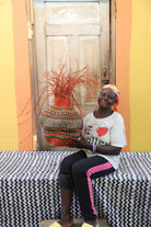Handwoven Bolga Baobab basket in rust-orange with multicolour band, held by a seated woman in a striped top.