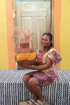 Handwoven Bolga Baobab basket with dark brown base and orange bands, held by a seated woman in a printed dress.