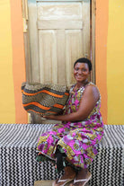 Handwoven Bolga wave basket in orange and dark wave stripes, held by a seated woman in a printed dress.