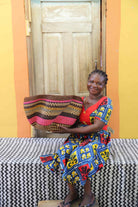Handwoven Bolga wave basket in pink and black wavy stripes, held by a seated woman in a printed dress.
