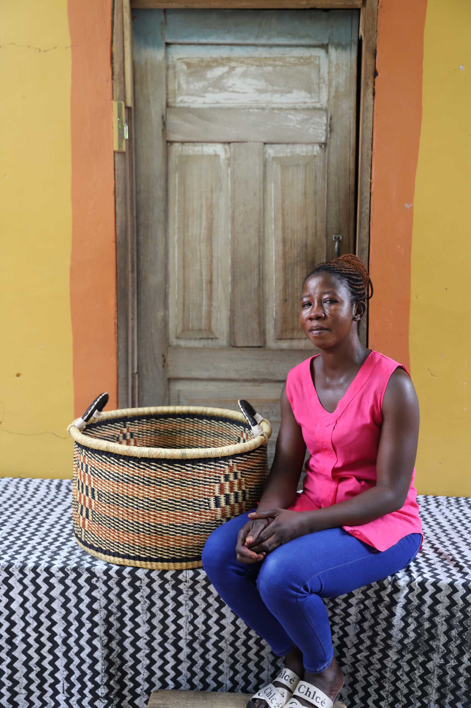 Handwoven Bolga storage basket in natural straw with orange and black stripes, styled beside a seated woman.