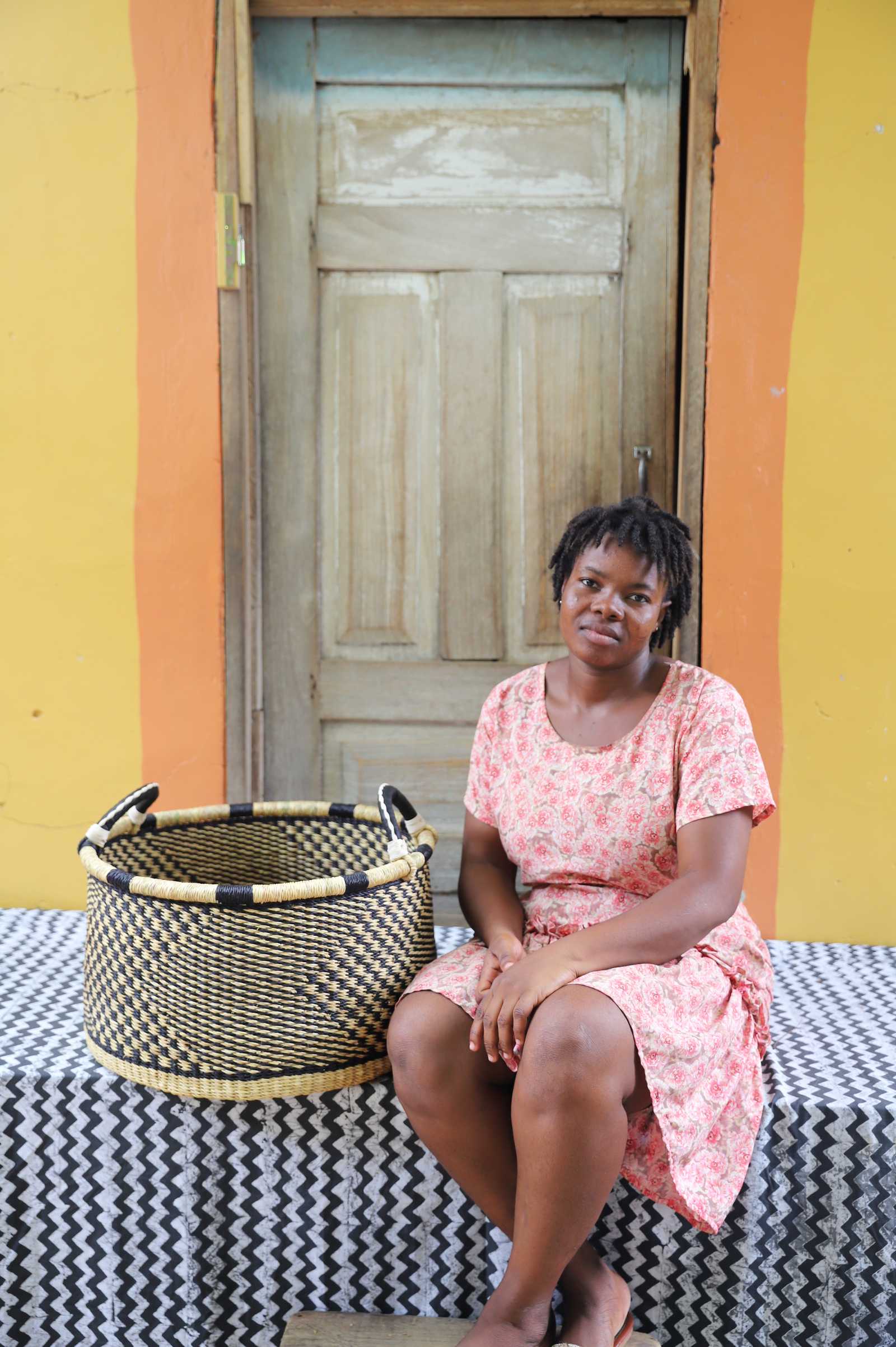 Handwoven Bolga storage basket in natural straw with a black geometric weave, styled beside a seated woman.