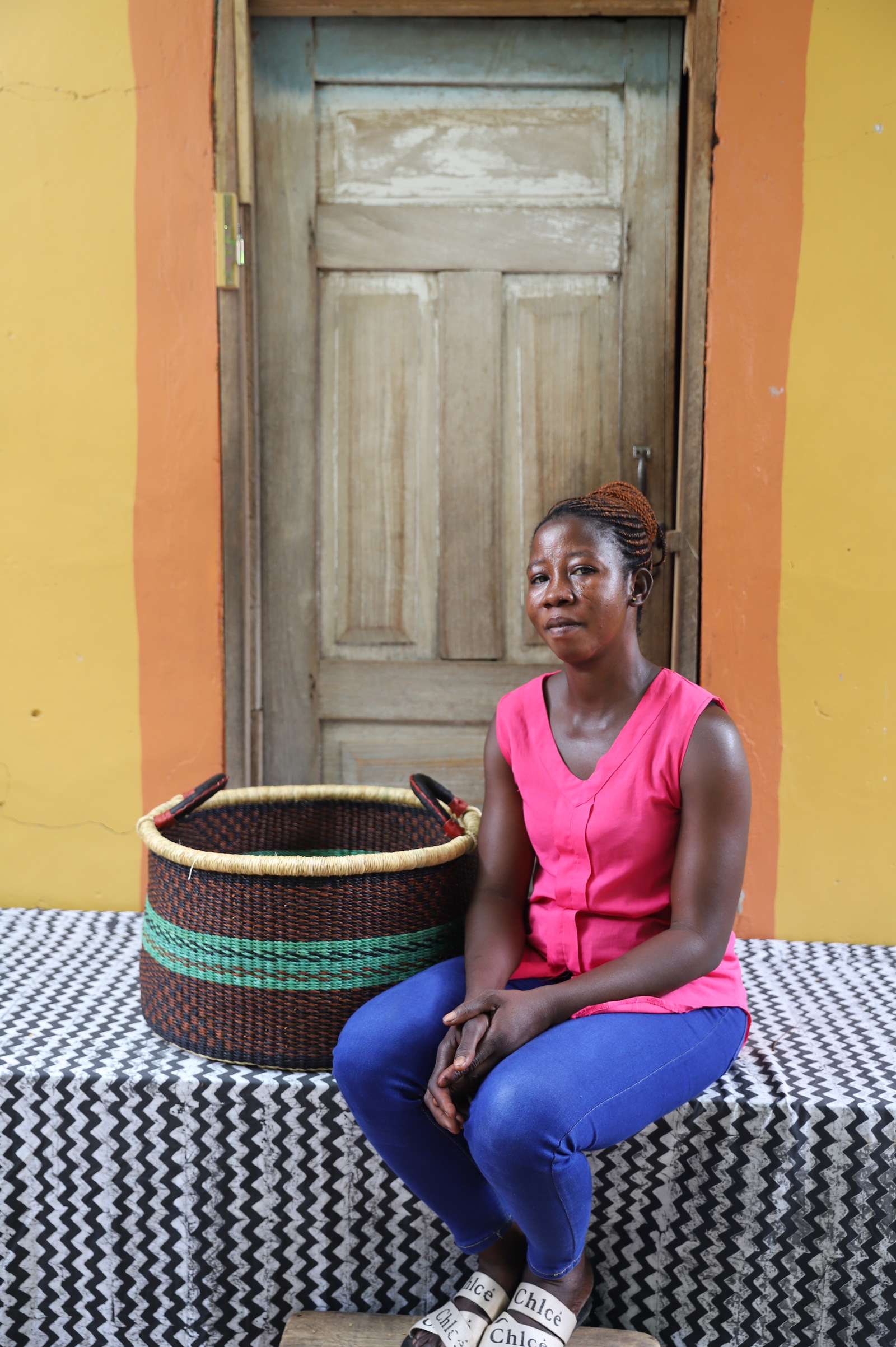 Handwoven Bolga storage basket in dark brown with green stripes, styled beside a seated woman in pink.
