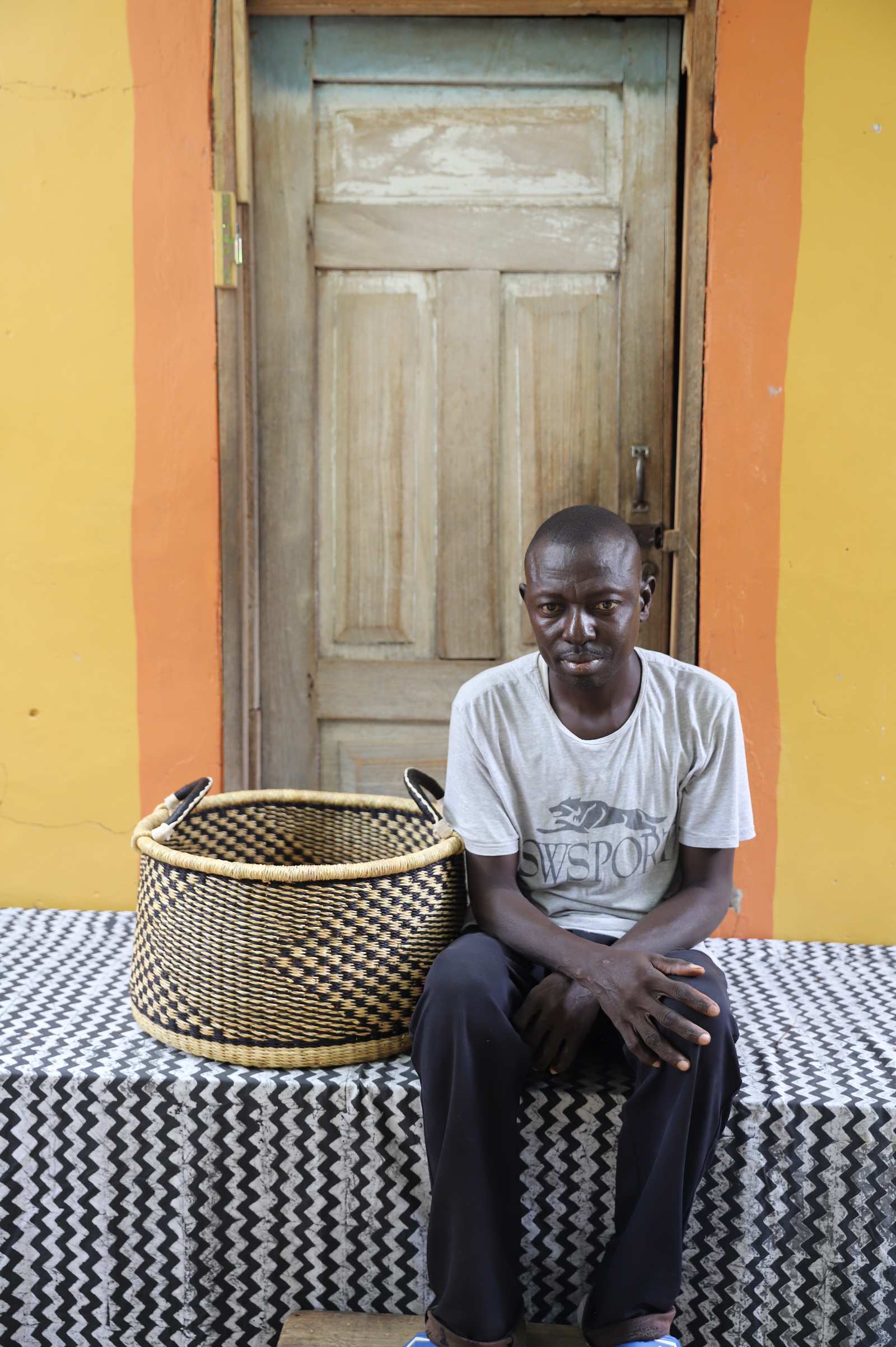 Handwoven Bolga storage basket in natural straw with a dark geometric weave, styled beside a seated man.