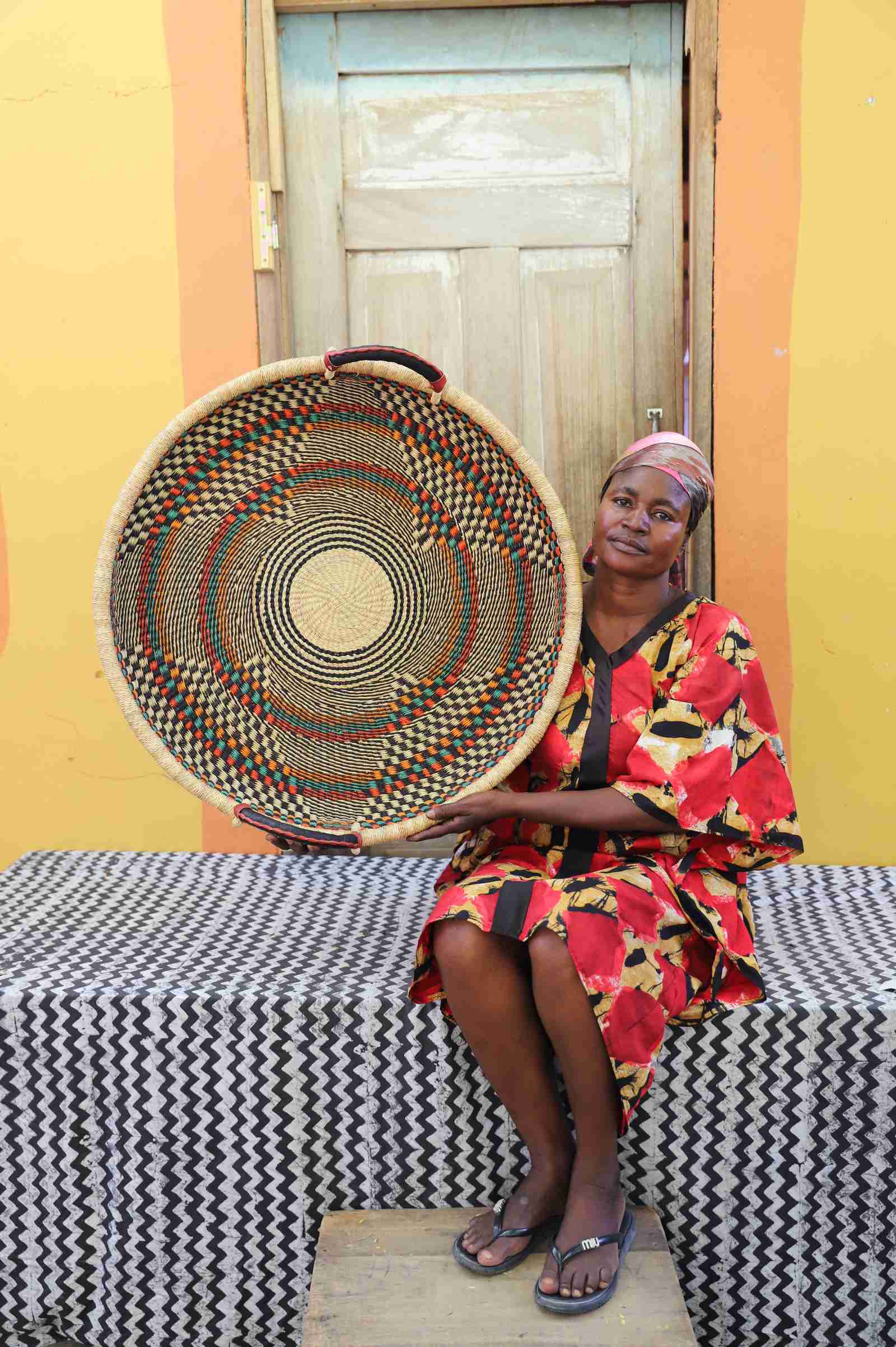 Large handwoven Bolga wall tray disc with dark radial star pattern, held by a seated woman in red.