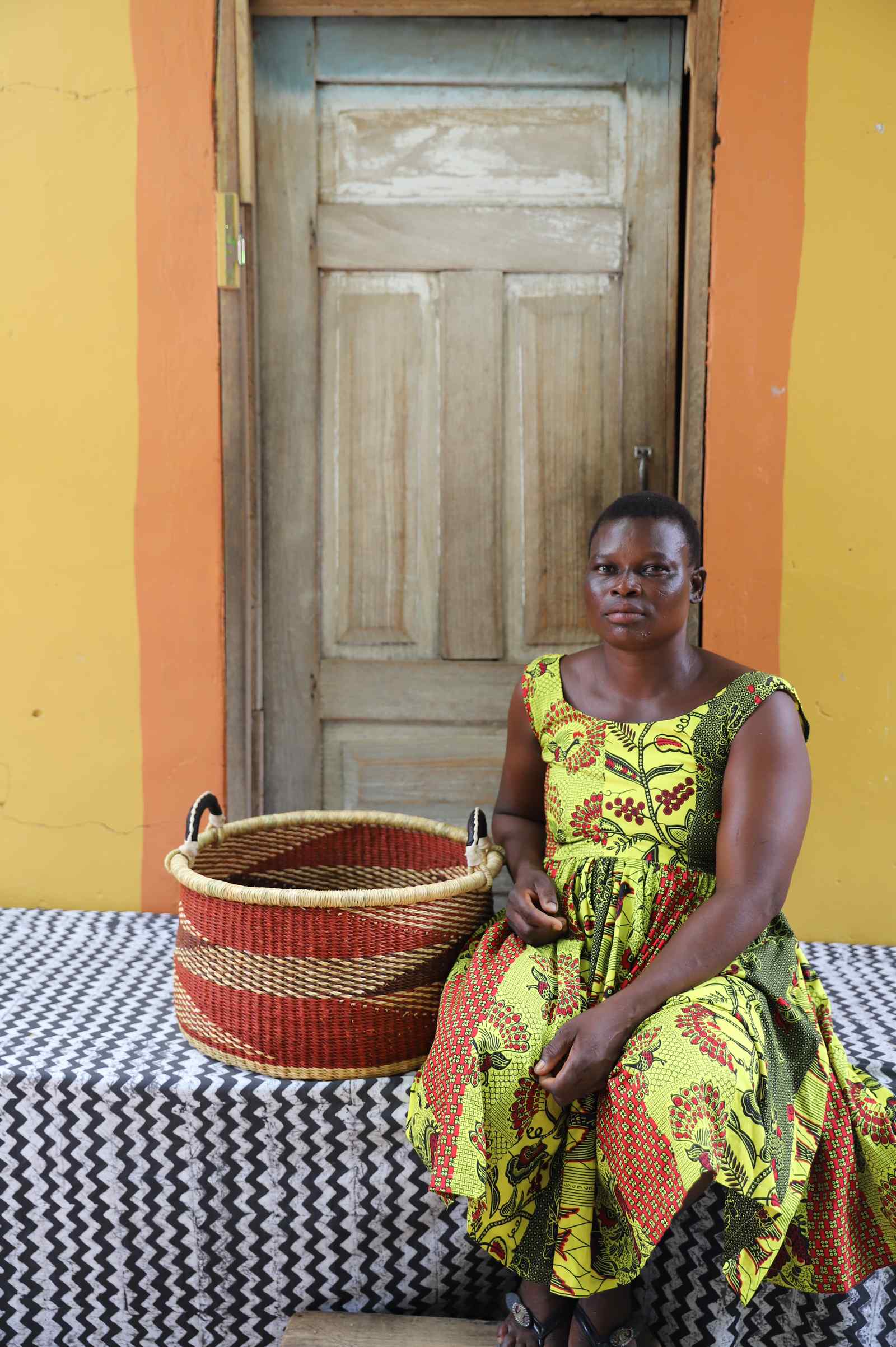 Handwoven Bolga storage basket in natural straw with red horizontal stripes, styled beside a seated woman.