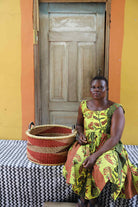Handwoven Bolga storage basket in natural straw with red horizontal stripes, styled beside a seated woman.