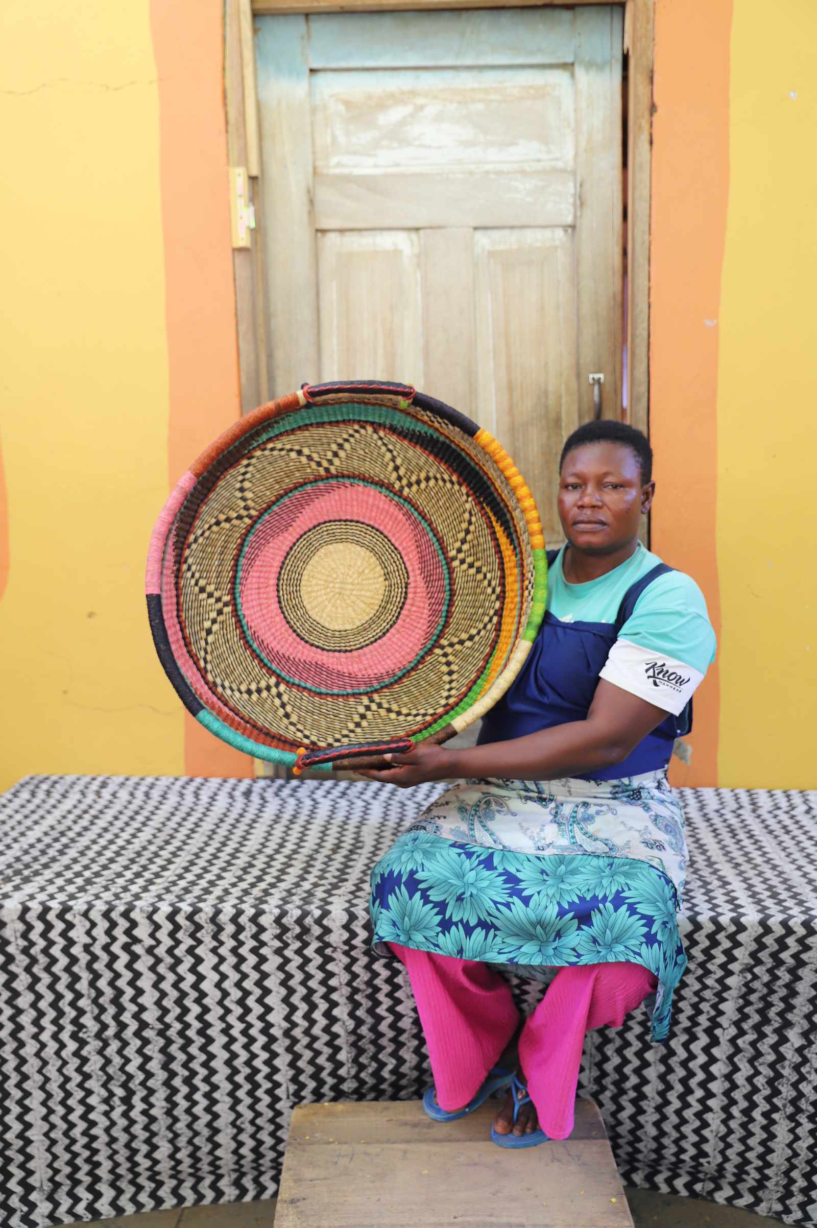 Medium handwoven Bolga wall tray disc with pink, red and orange rings, held by a seated woman in teal.