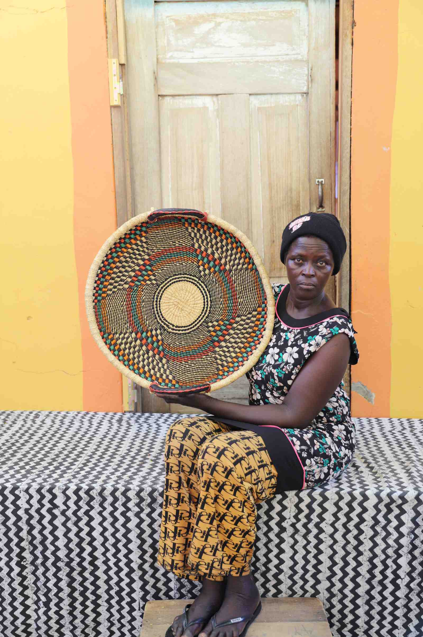 Handwoven Bolga wall tray disc with fine dark concentric bands, held by a seated woman in floral.