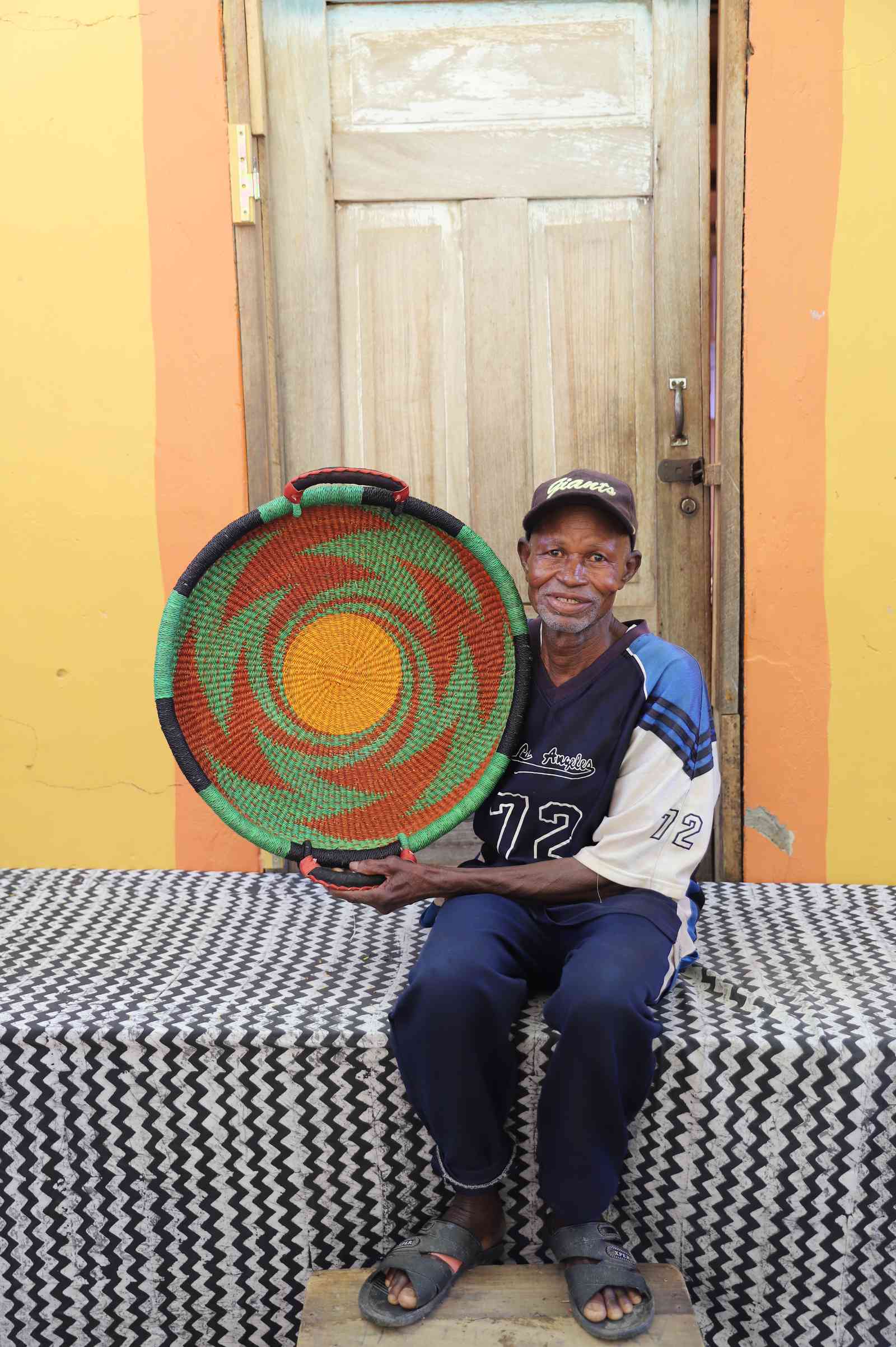 Handwoven Bolga wall tray disc with green rim and orange swirl, held by a seated man in a jersey.