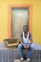 Medium handwoven Bolga pet bed in natural with black herringbone weave, beside a seated man in white.