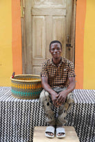 Woven Tub (Small) with man weaver handwoven in Ghana sitting on black and white cloth and wooden door in background