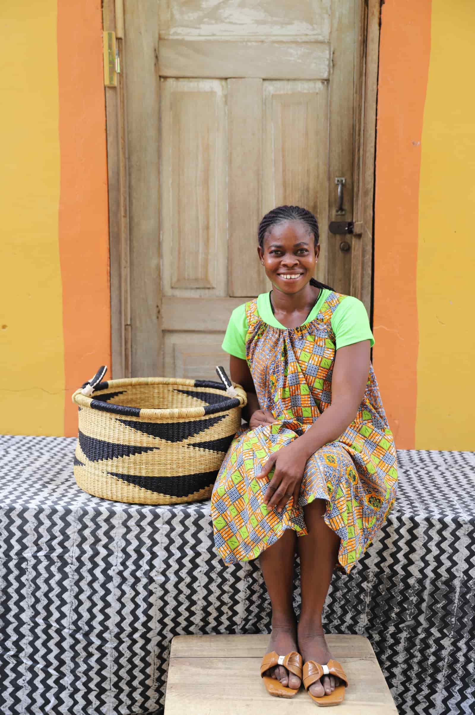 Woven Tub (Small) with woman weaver handwoven in Ghana sitting on black and white cloth and wooden door in background